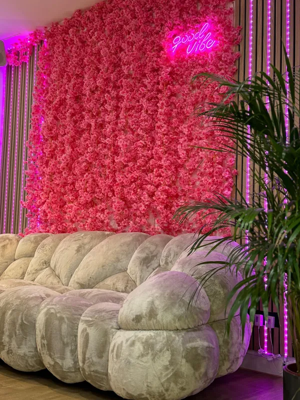 Wartebereich im Studio mit pinker Blütenwand, Neonschriftzug und geschwungenem Sofa