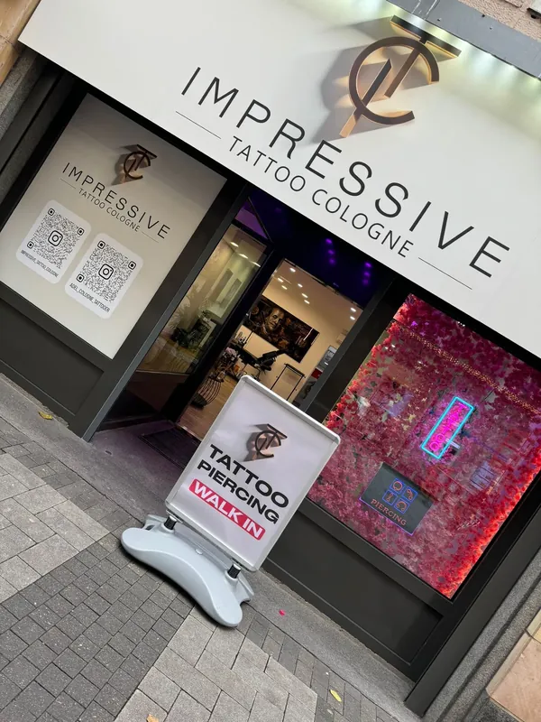 Eingang des Studios an der Breite Straße mit weißem Schild, Monogramm und einem Aufsteller mit der Aufschrift Tattoo Piercing Walk in