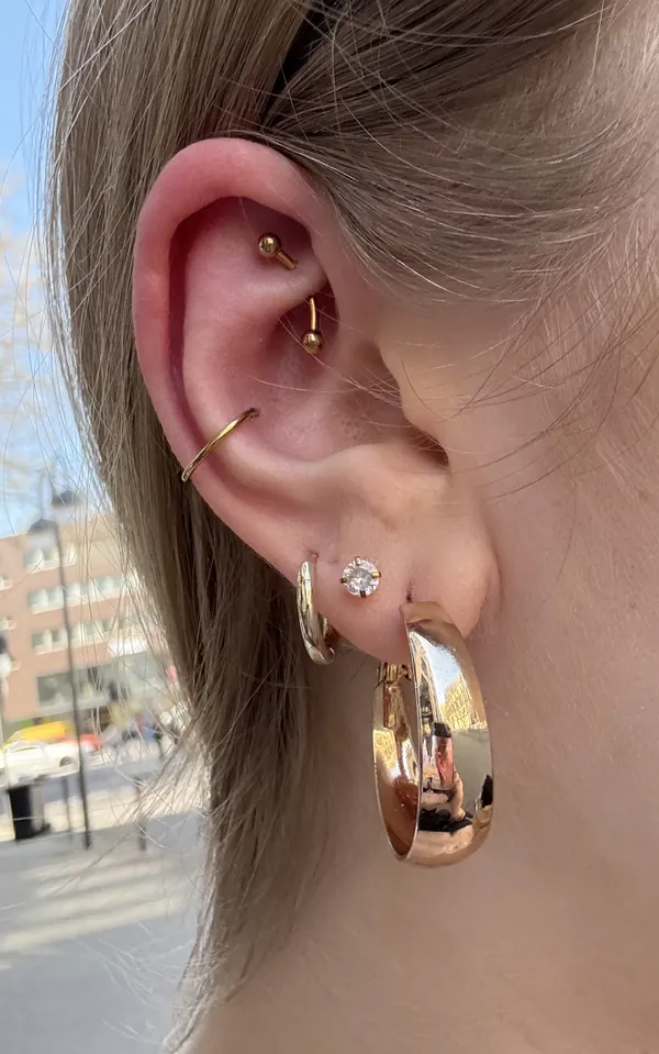 Mehrere Ohrpiercings mit goldenem Schmuck, darunter Helix und Creolen